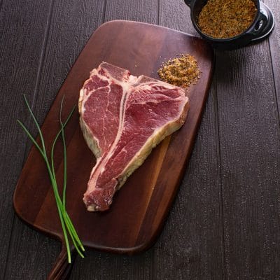Un chuletón con hueso sobre una tabla de madera oscura, con cebollín al lado