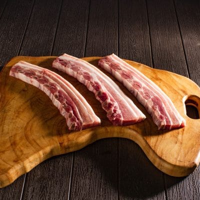 Cuatro costillas de cerdo alineadas sobre una tabla de madera clara
