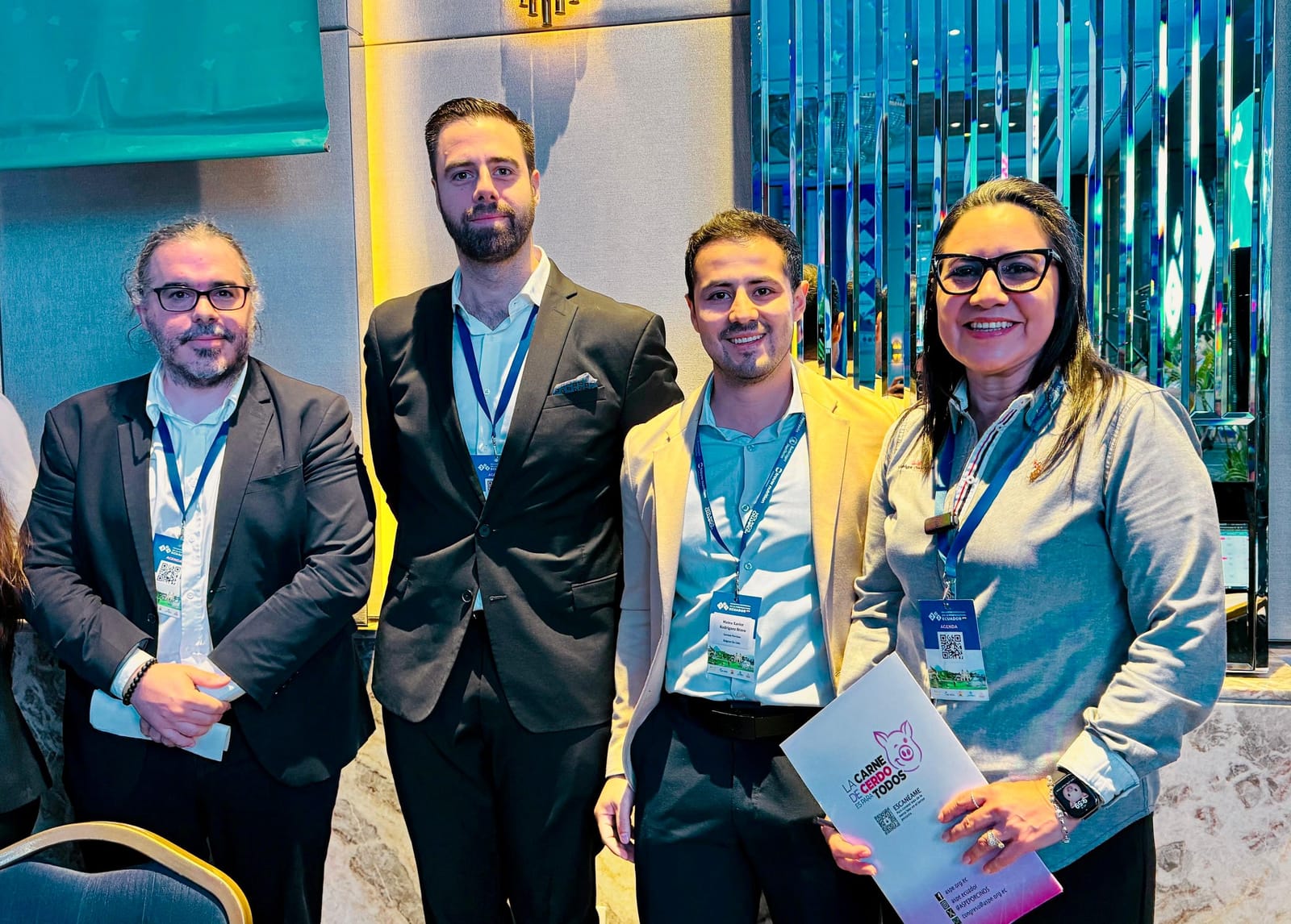 Cuatro asistentes con credenciales del encuentro, uno de ellos sostiene el programa del evento